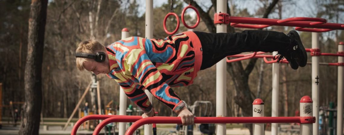 Young adult man exercises on outdoor gym bars in a colorful outfit in Vilnius, Lithuania.